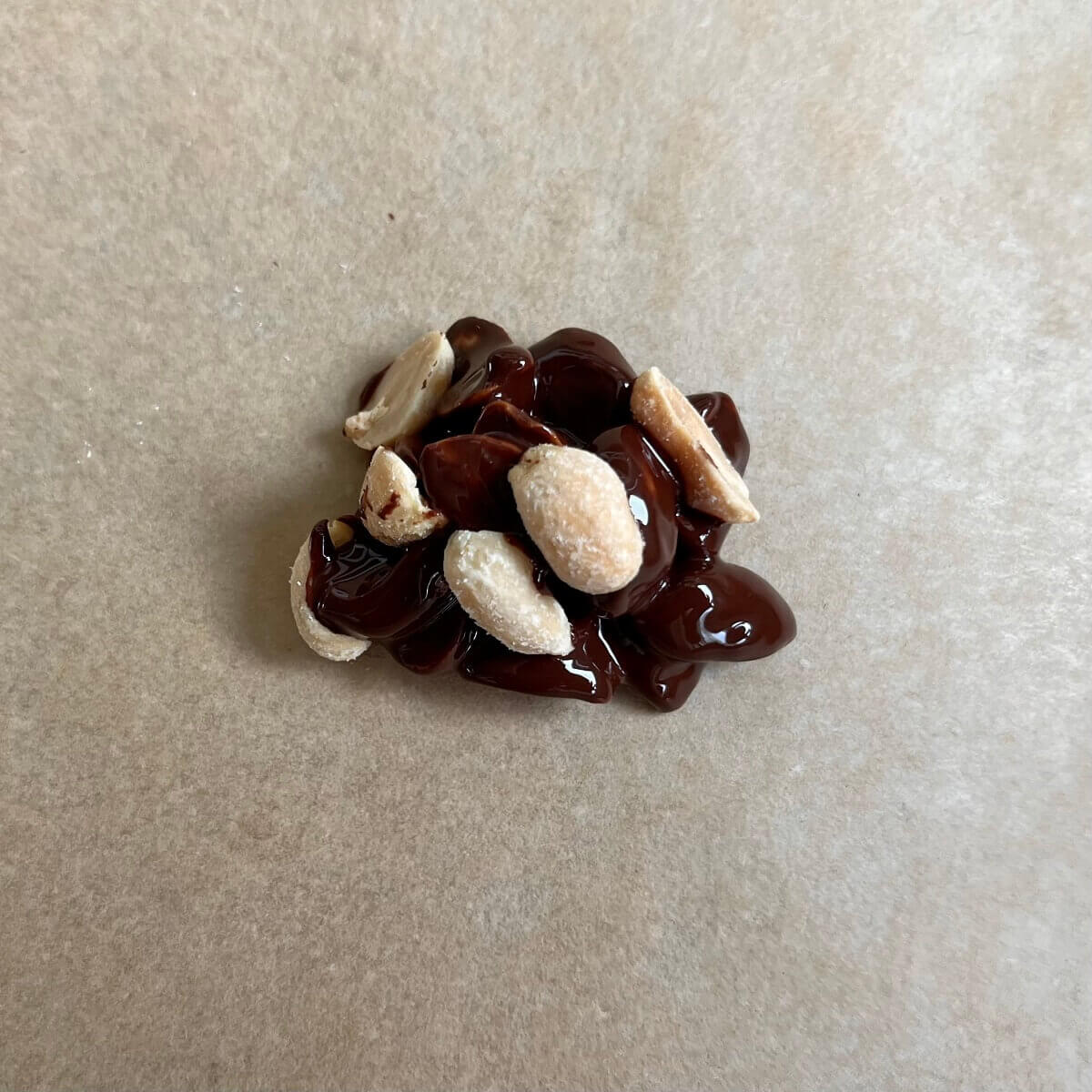 A cluster of melted dark chocolate and peanuts on a sheet pan lined with parchment paper.