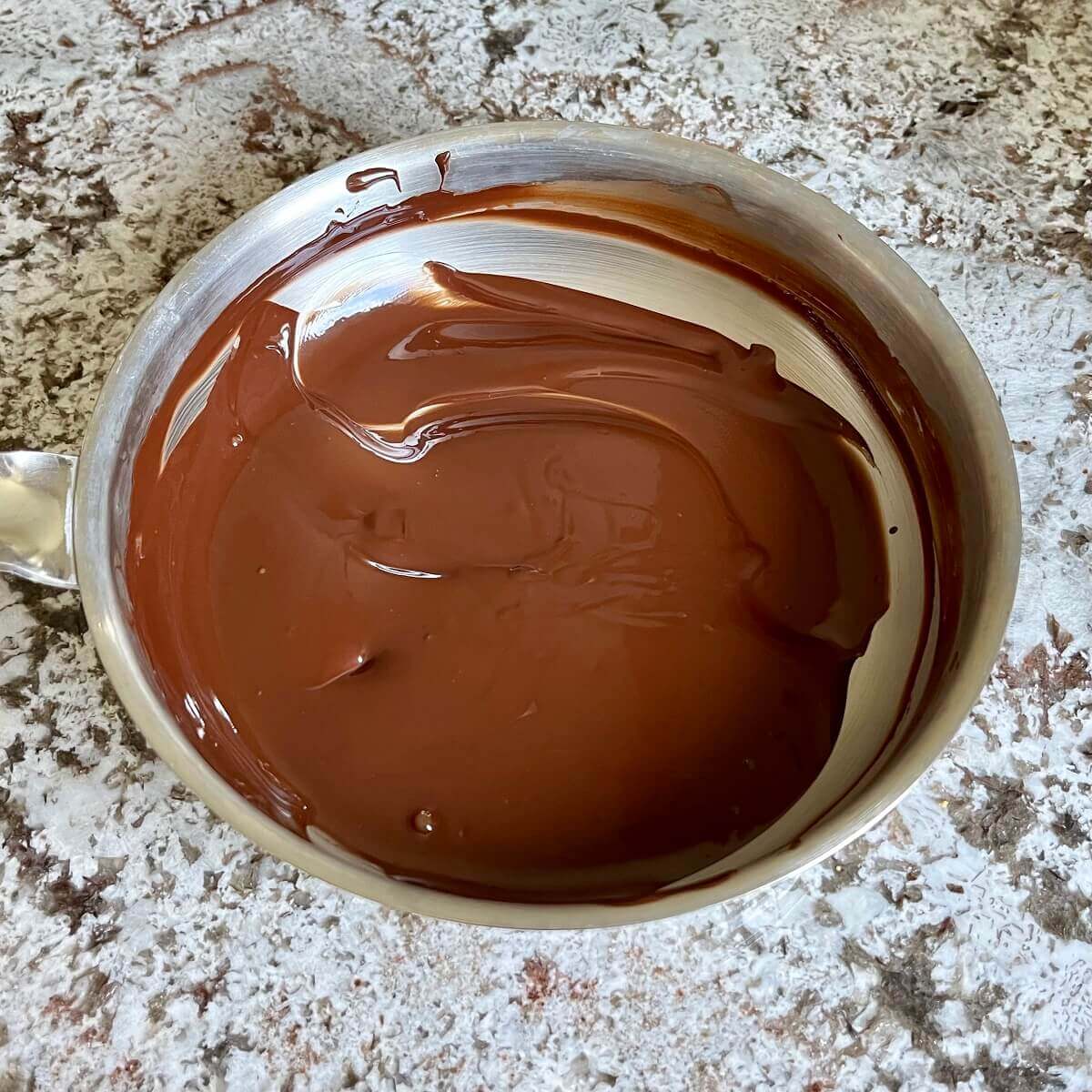 Melted dark chocolate in a stainless steel pan.