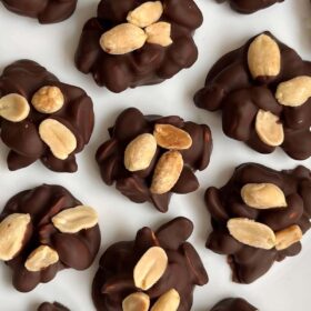 Several dark chocolate peanut clusters on a white plate.
