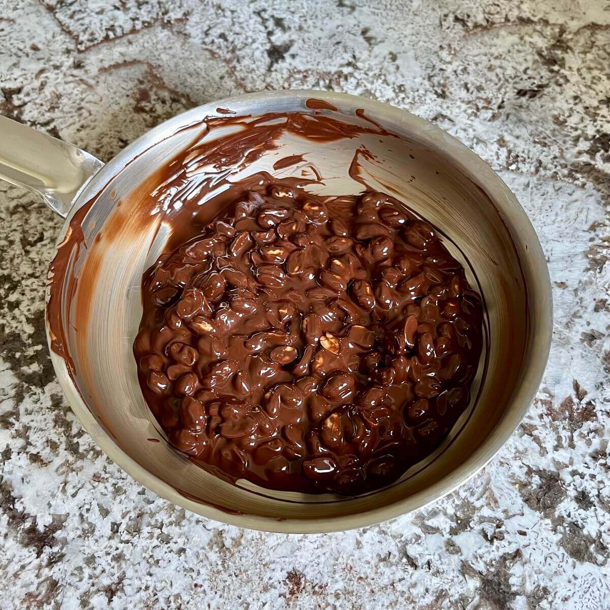 Peanuts covered in melted dark chocolate in a steel pan.