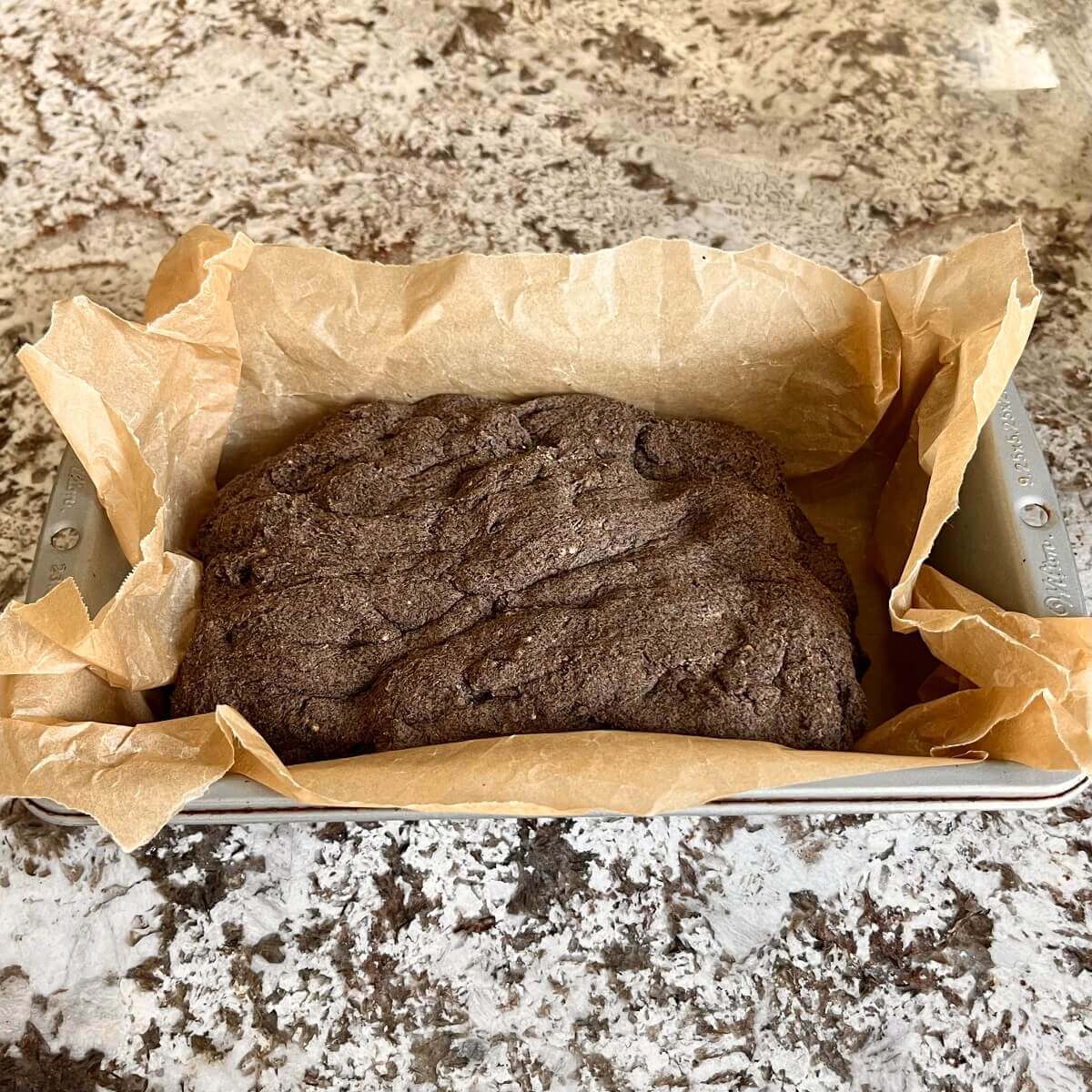 Bread dough in a loaf pan lined with parchment paper.