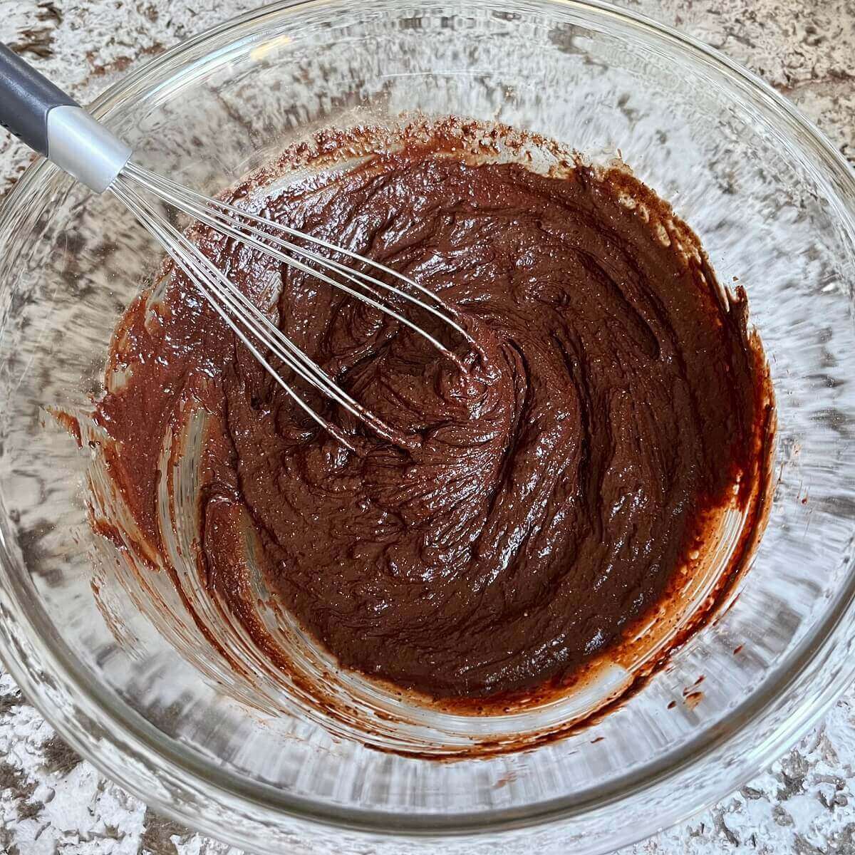 Wet ingredients for brownies in a glass mixing bowl with a whisk.