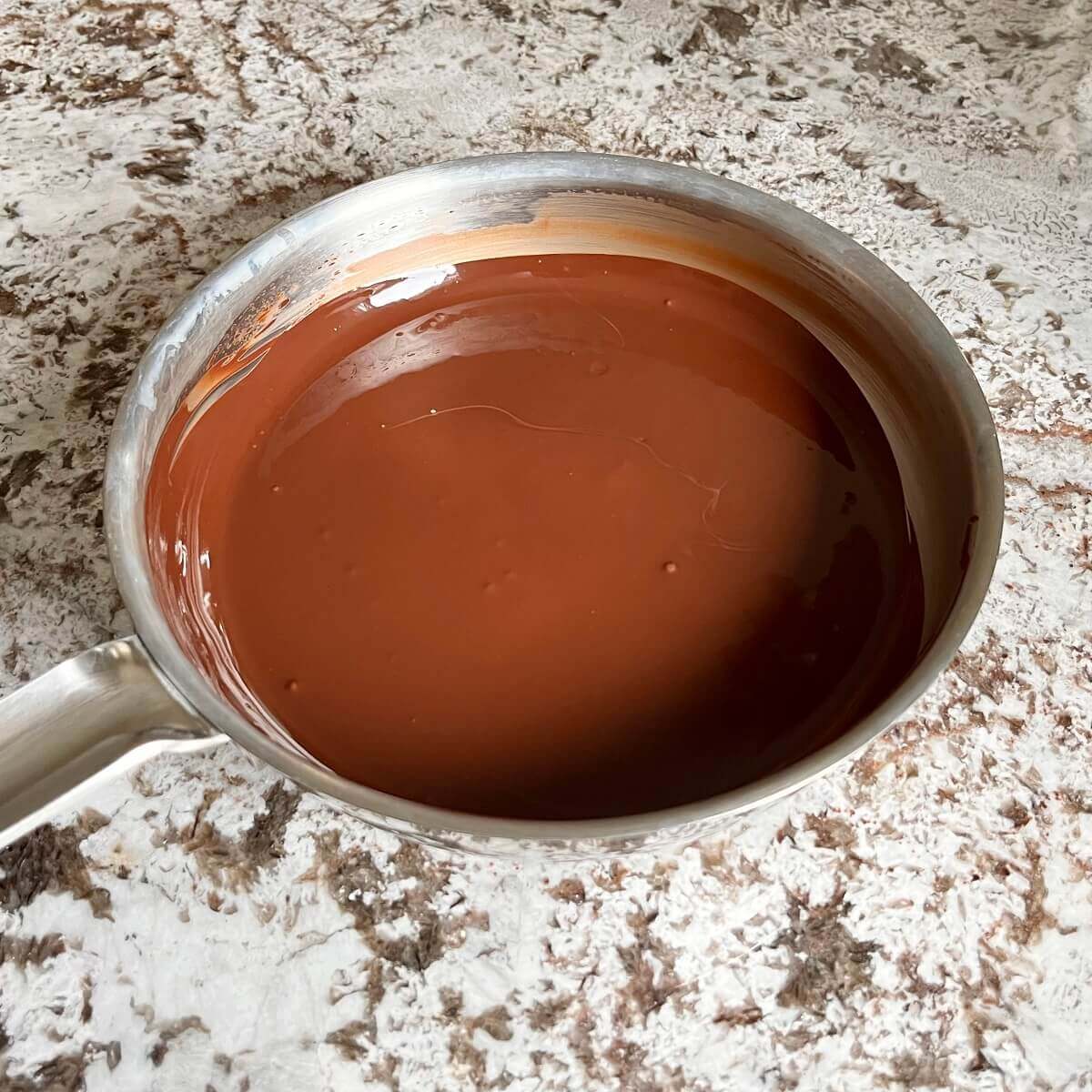 Melted dark chocolate in a steel pan on a granite counter.