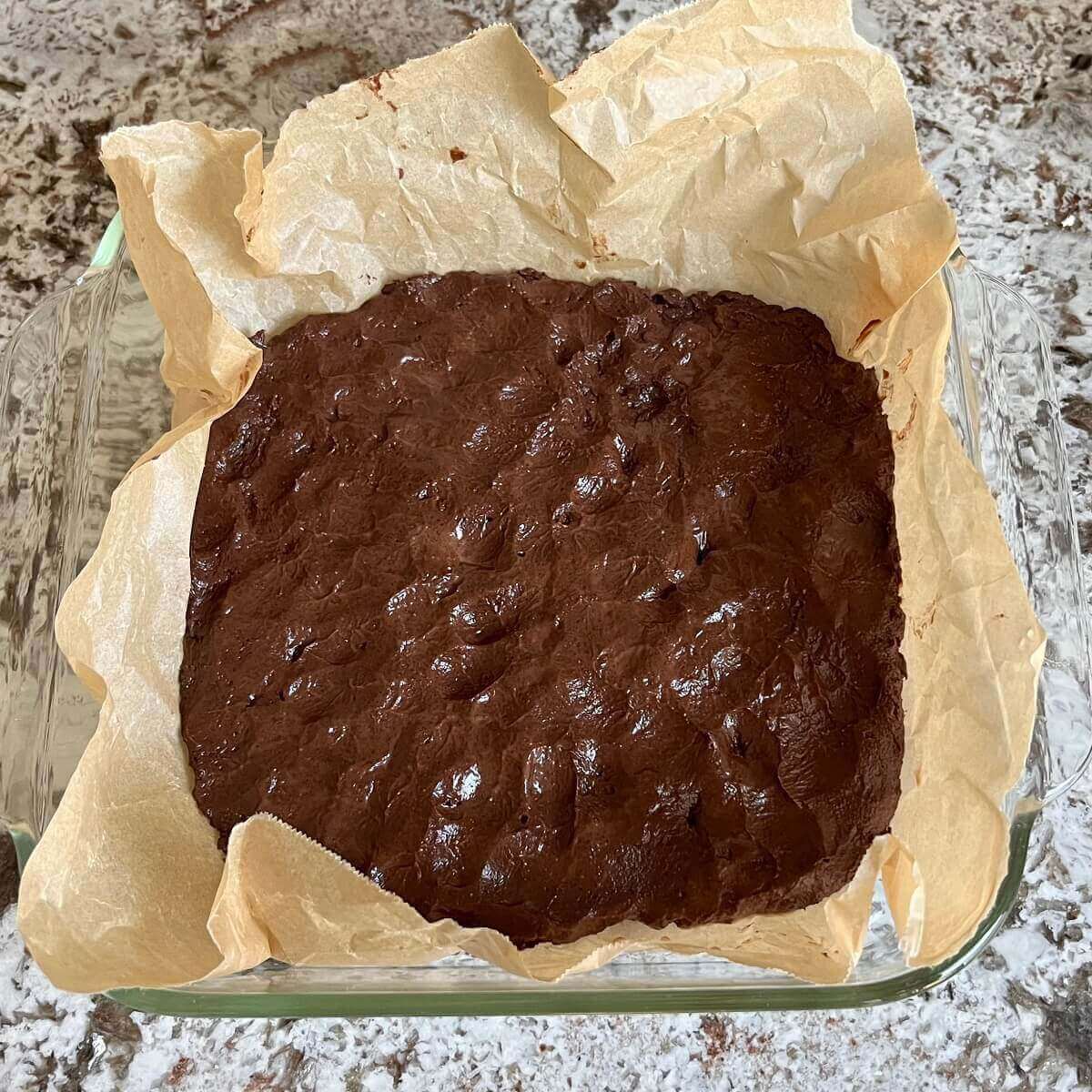 Raw brownies in a baking dish lined with parchment paper.