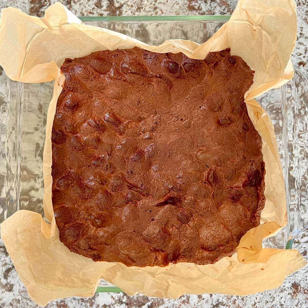 Brownie batter in a glass dish lined with parchment paper.