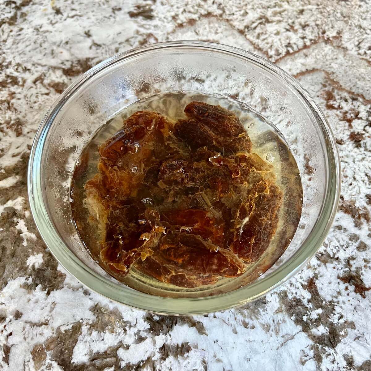 Dates soaking in hot water in a glass bowl.