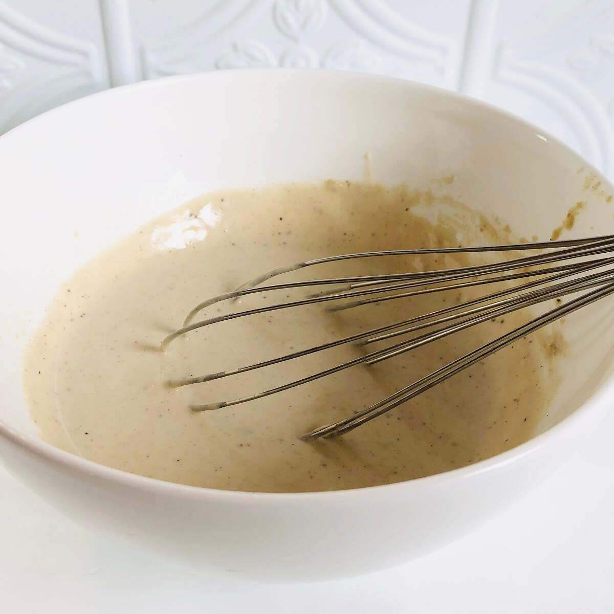 Creamy tahini sauce in a white bowl with a whisk.