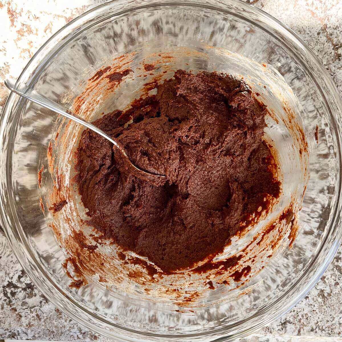 Thick brownie batter in a glass mixing bowl.