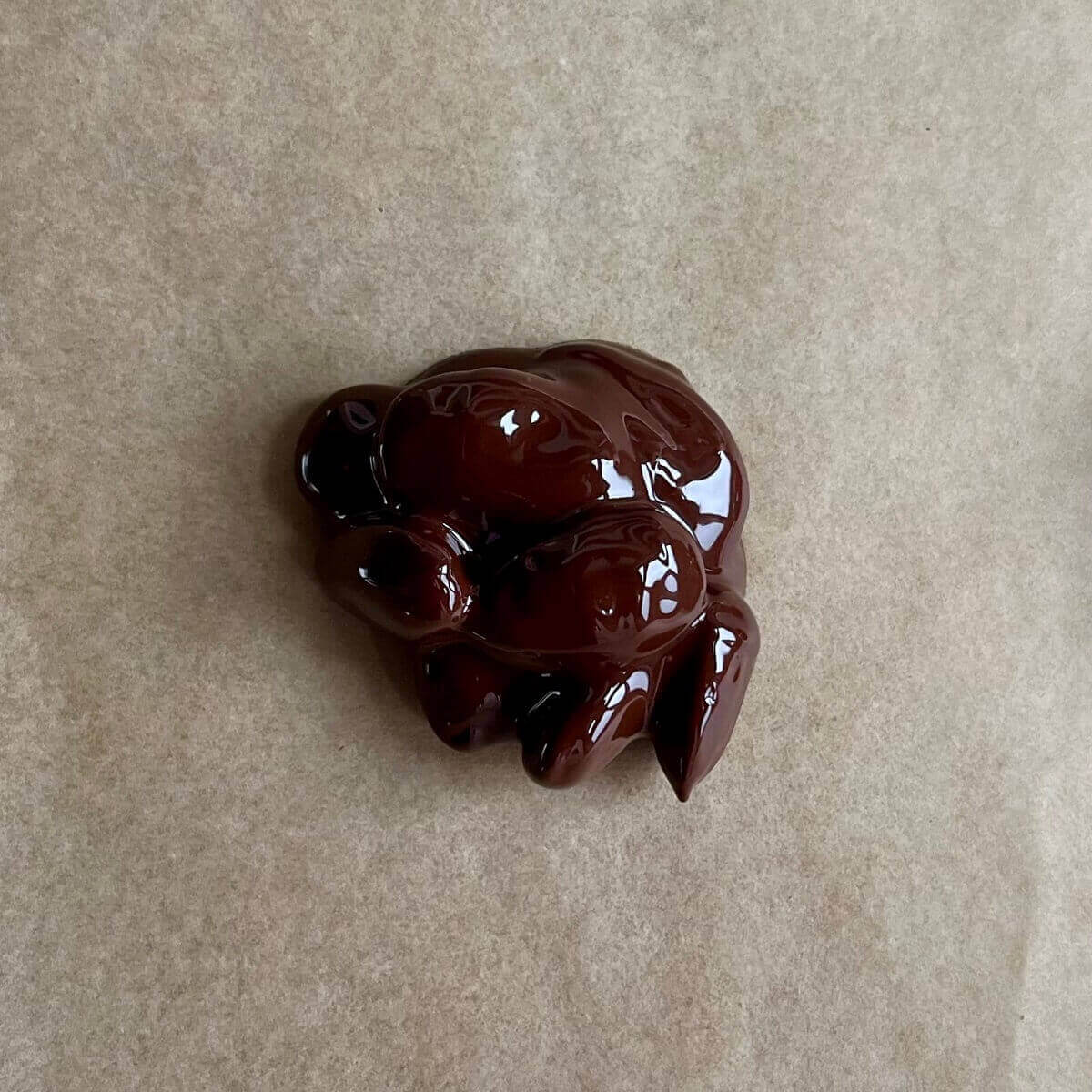 A small pile of almonds covered in melted chocolate on a piece of parchment paper.