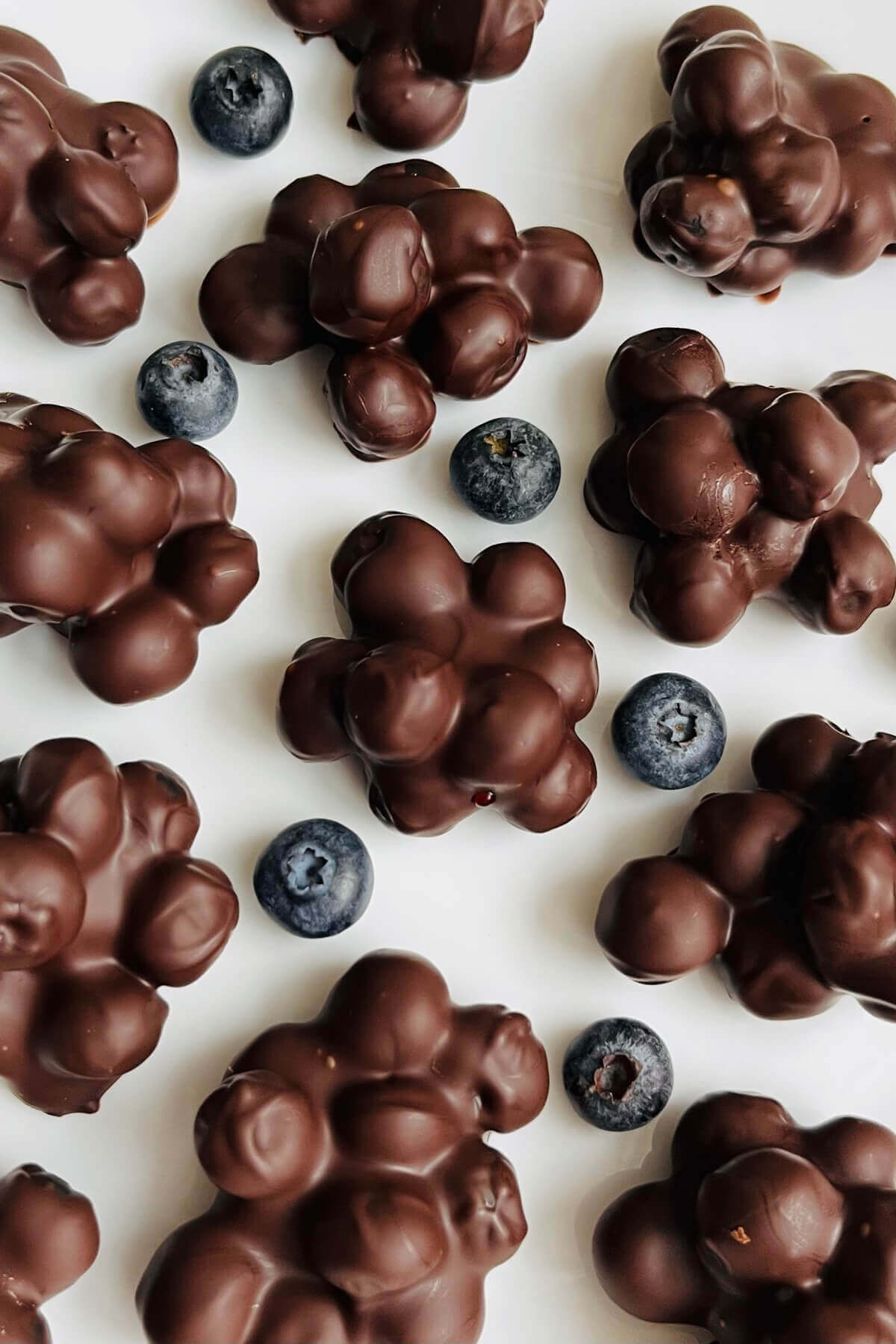 Chocolate blueberry clusters and fresh blueberries on a plate.