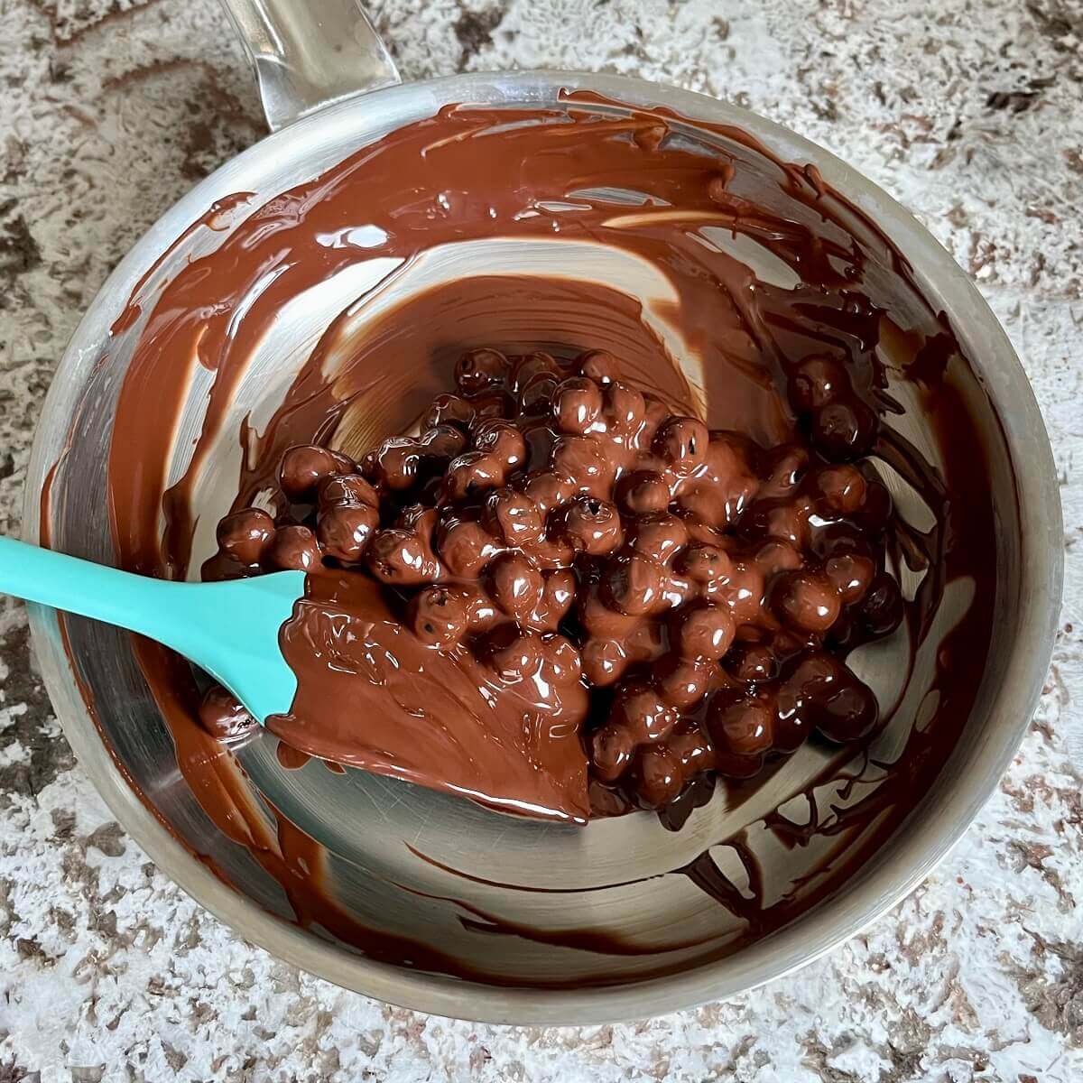 A mixture of melted chocolate and fresh blueberries in a pan.