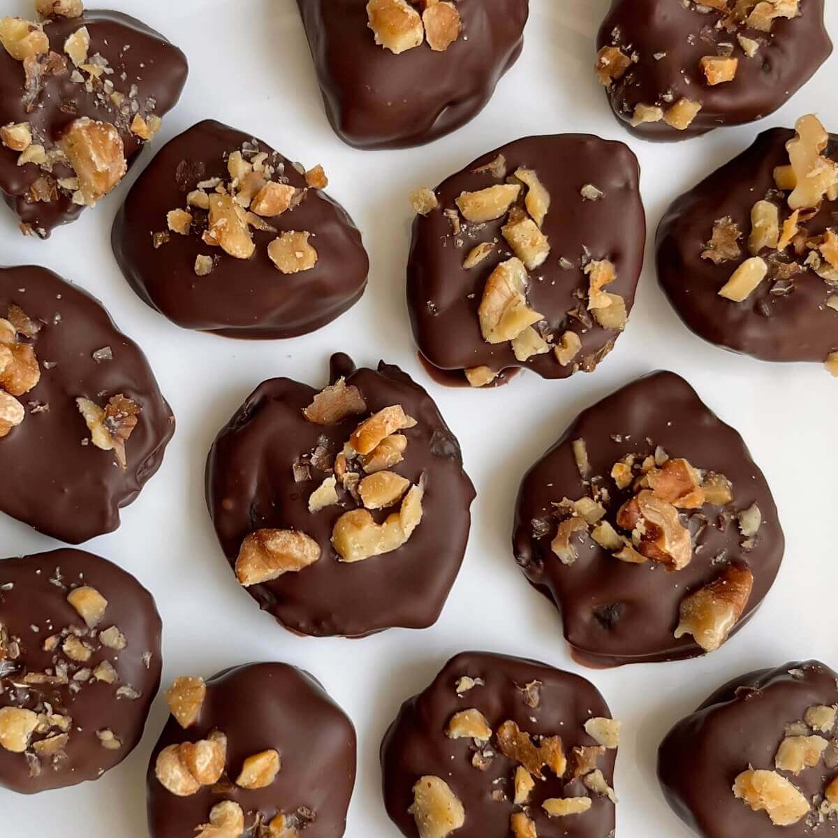 Chocolate covered prunes sprinkled with chopped walnuts on a white plate.