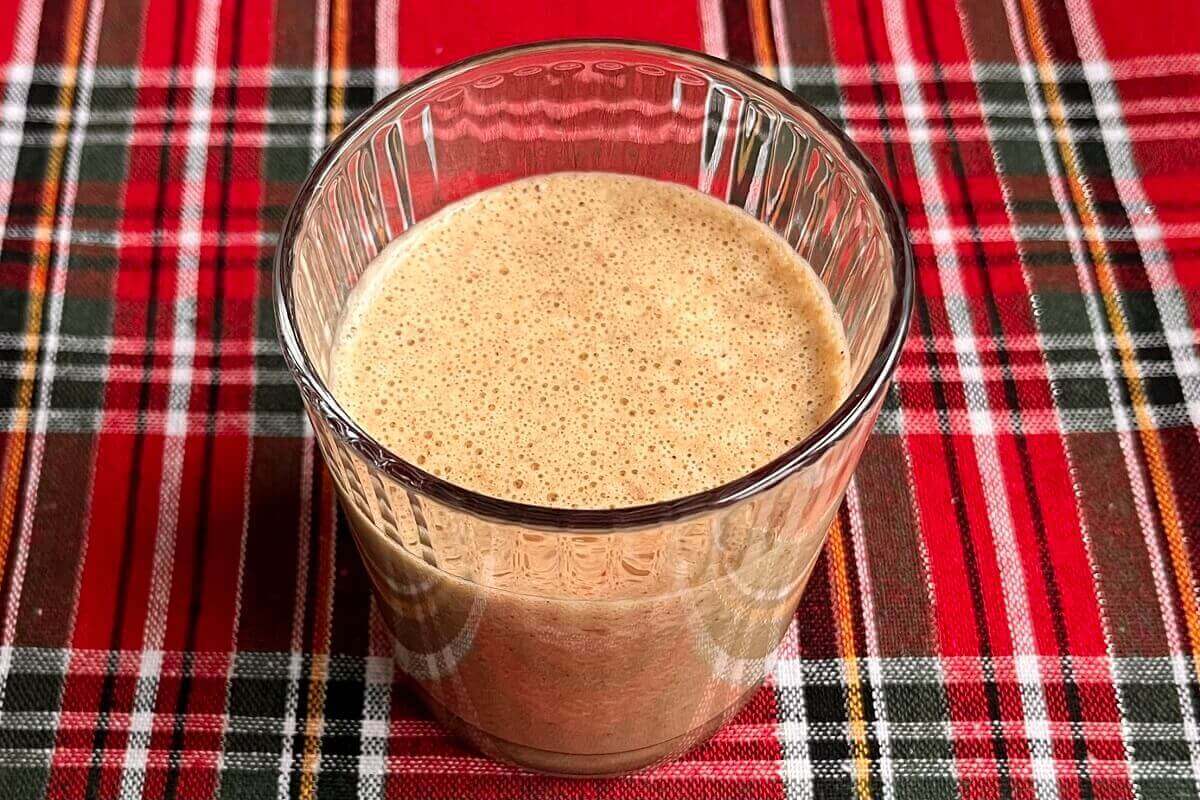 A creamy smoothie in a ribbed glass on a plaid placemat.