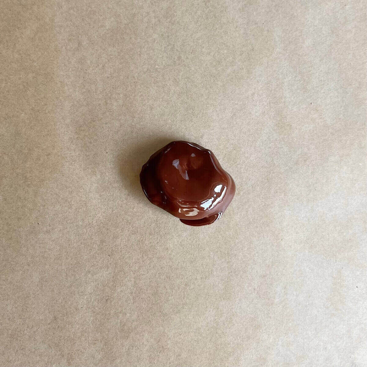 A prune coated in melted dark chocolate on parchment paper.
