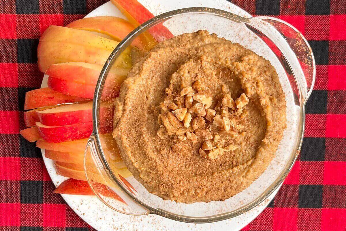Gingerbread dip in a glass bowl next to some apple slices.