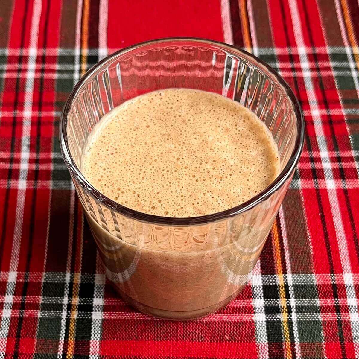 A gingerbread smoothie in a glass on a plaid placemat.