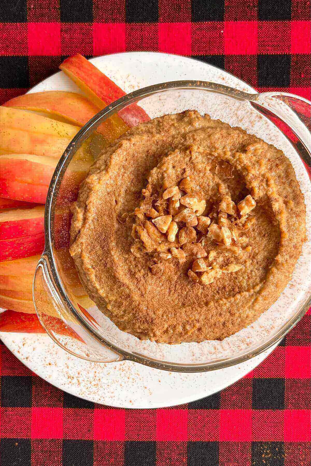Hummus in a glass bowl next to apple slices.