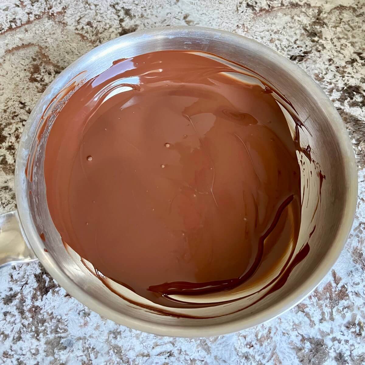 Melted dark chocolate in a stainless steel pan.