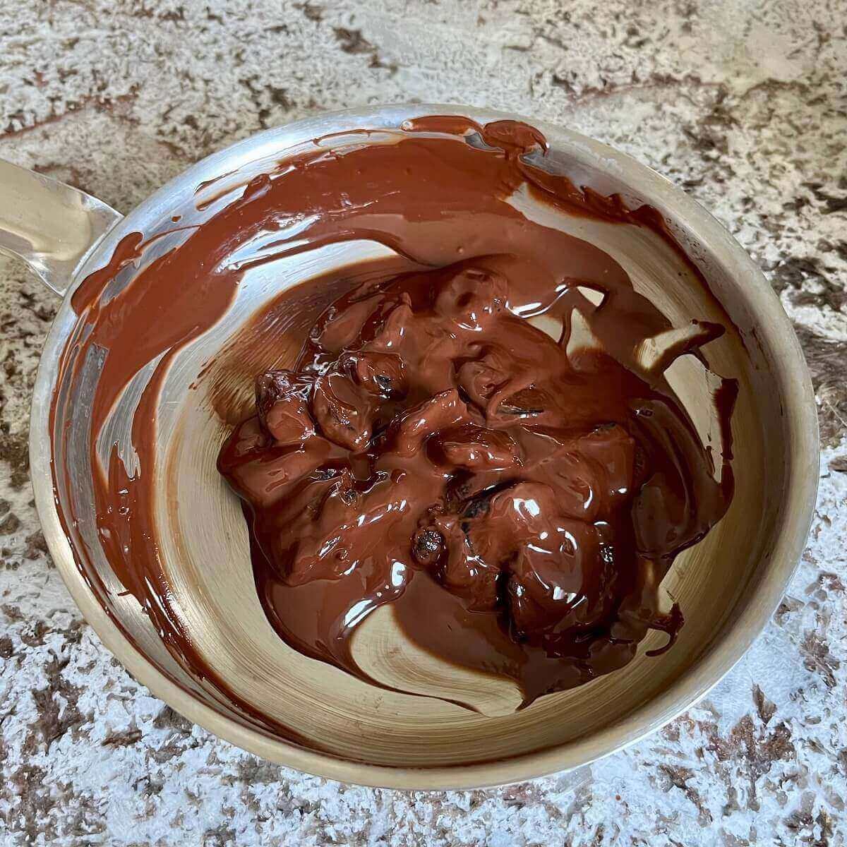 Prunes covered in melted chocolate in a steel pan.