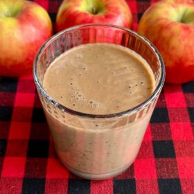 An apple protein smoothie in a glass with three apples in the background.