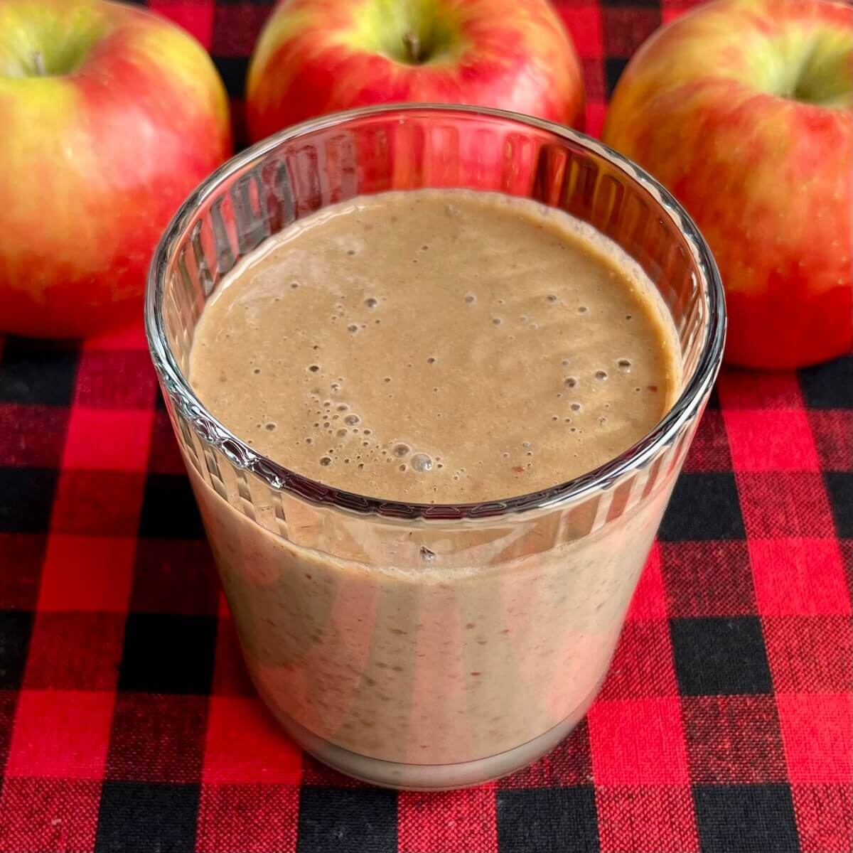 An apple protein smoothie in a glass with three apples in the background.