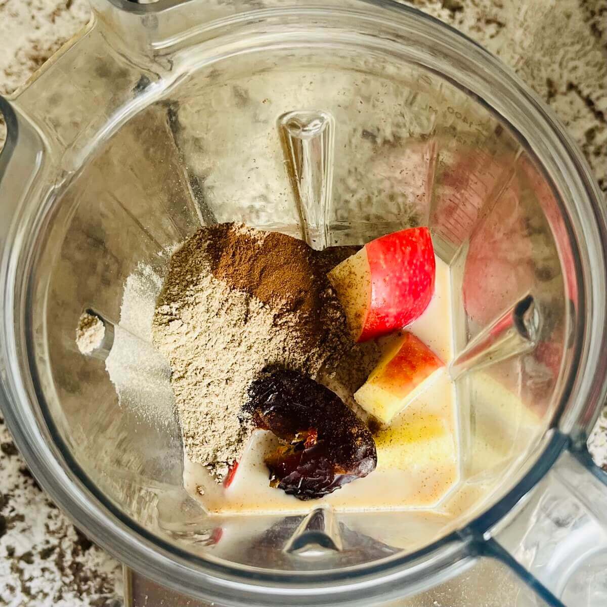 Chopped apples, protein powder, cinnamon, soy milk, and a date in a blender.