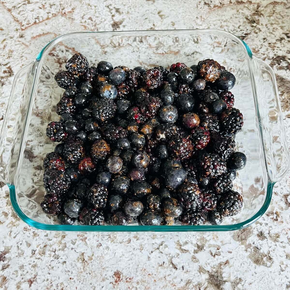 blackberries, blueberries, and other ingredients in a glass square baking dish.