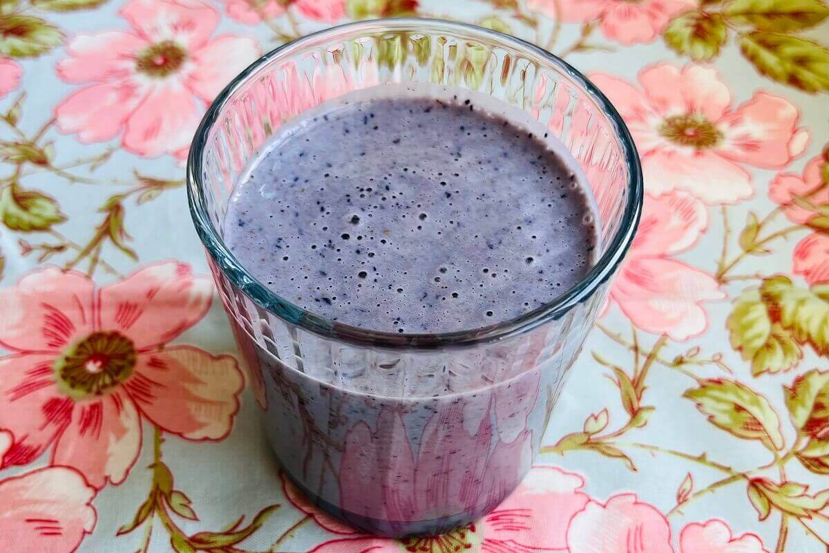 A blueberry smoothie in a glass on a floral placemat.