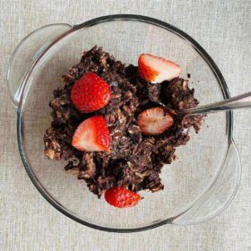 Vegan brownie baked oatmeal with sliced strawberries on top in a glass bowl.