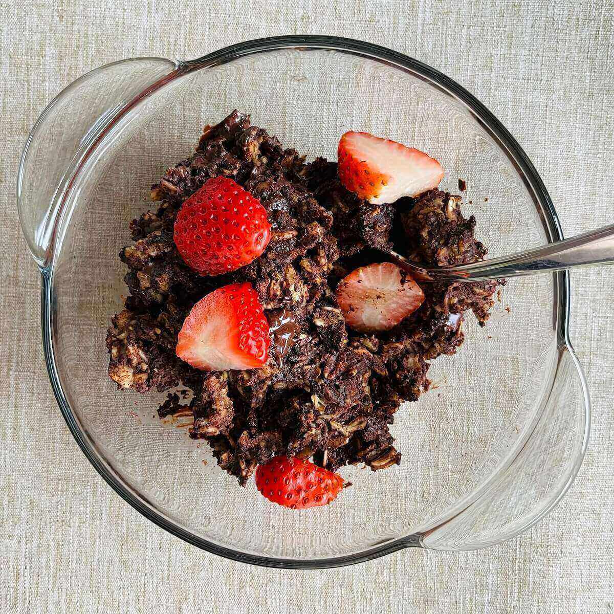 Vegan brownie baked oatmeal with sliced strawberries on top in a glass bowl.