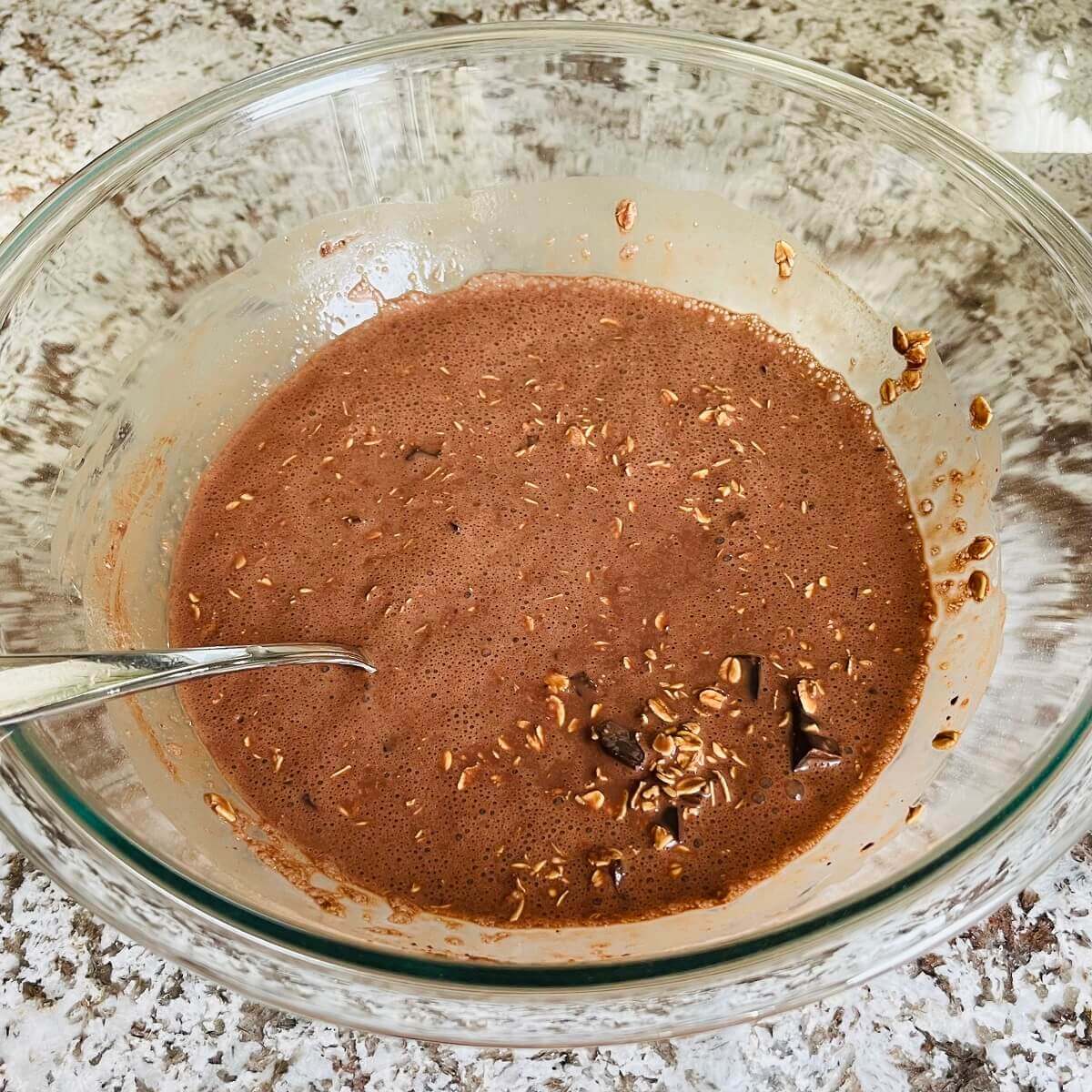 Ingredients for brownie baked oatmeal in a glass mixing bowl.