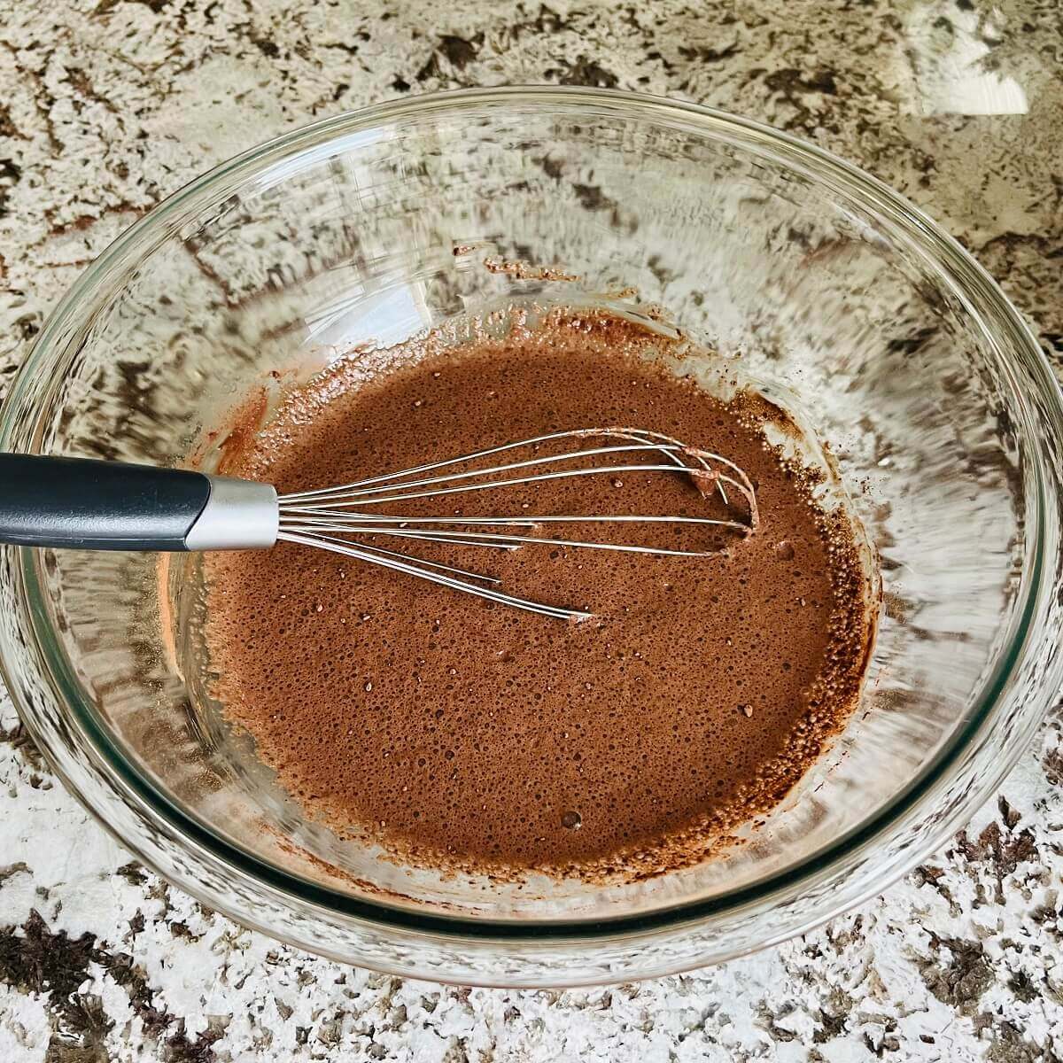 Brown batter in a glass mixing bowl with a whisk.