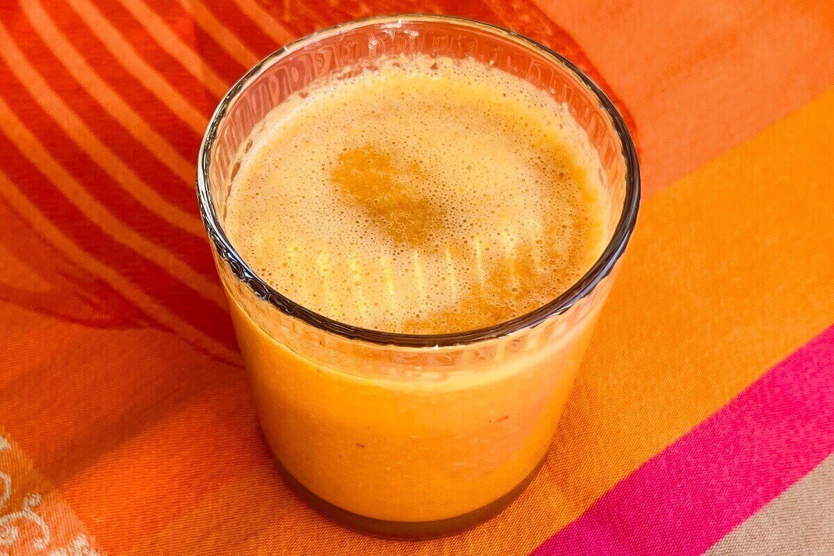 A carrot smoothie in a glass on a colorful cloth.