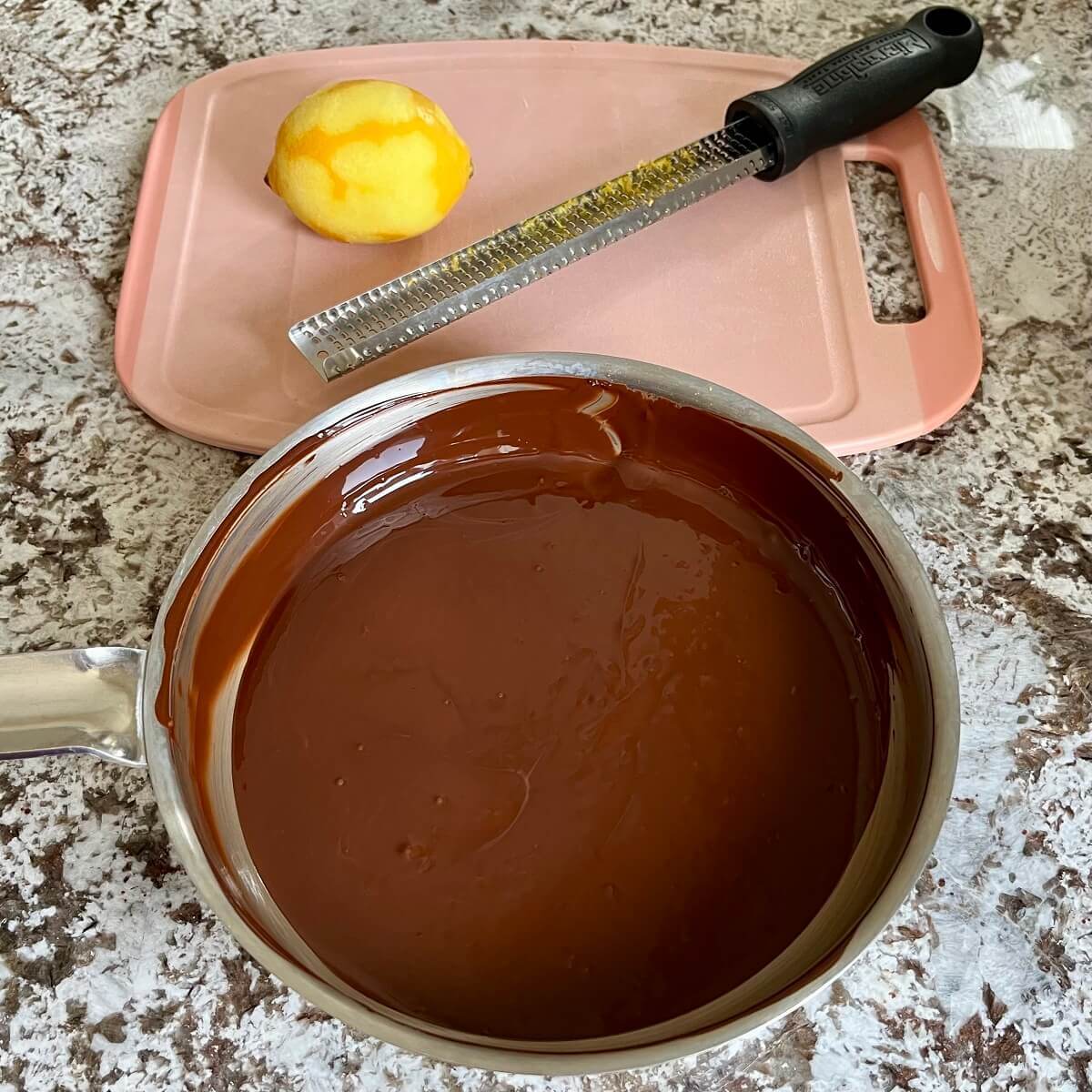 A pan of melted chocolate next to a lemon and zester on a cutting board.