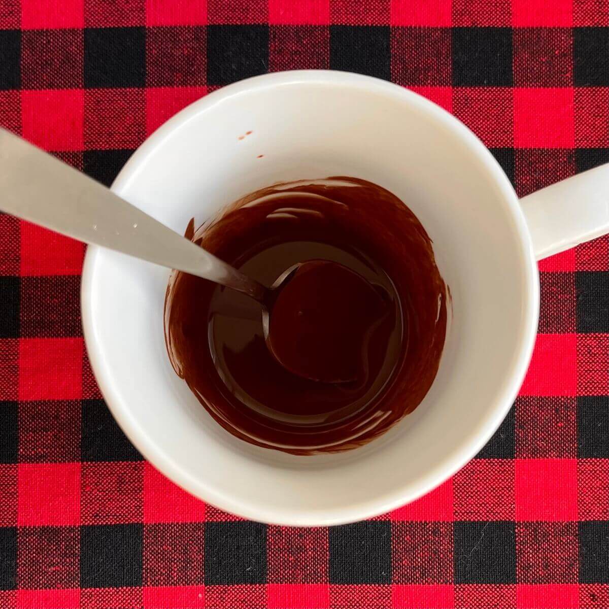 Cocoa powder dissolved in boiling water in a white mug with a spoon.