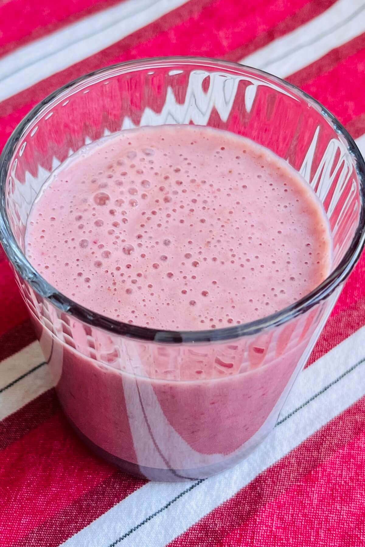 A date and strawberry smoothie in a glass on a striped tea towel.