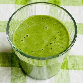A frozen kale smoothie in a glass on a green gingham cloth.
