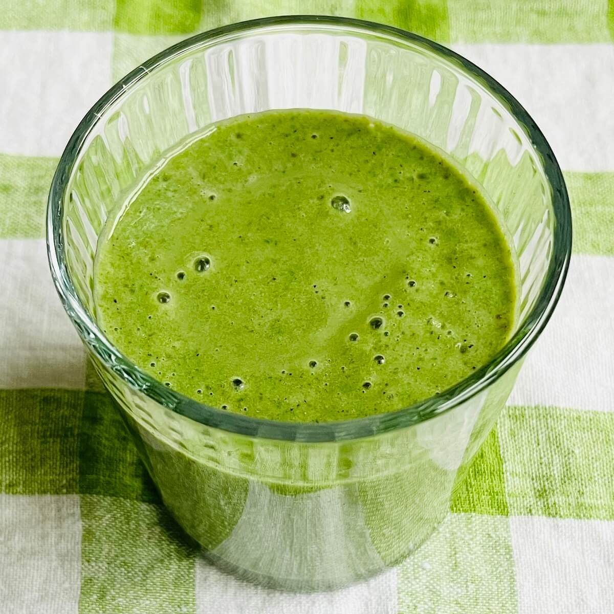 A frozen kale smoothie in a glass on a green gingham cloth.