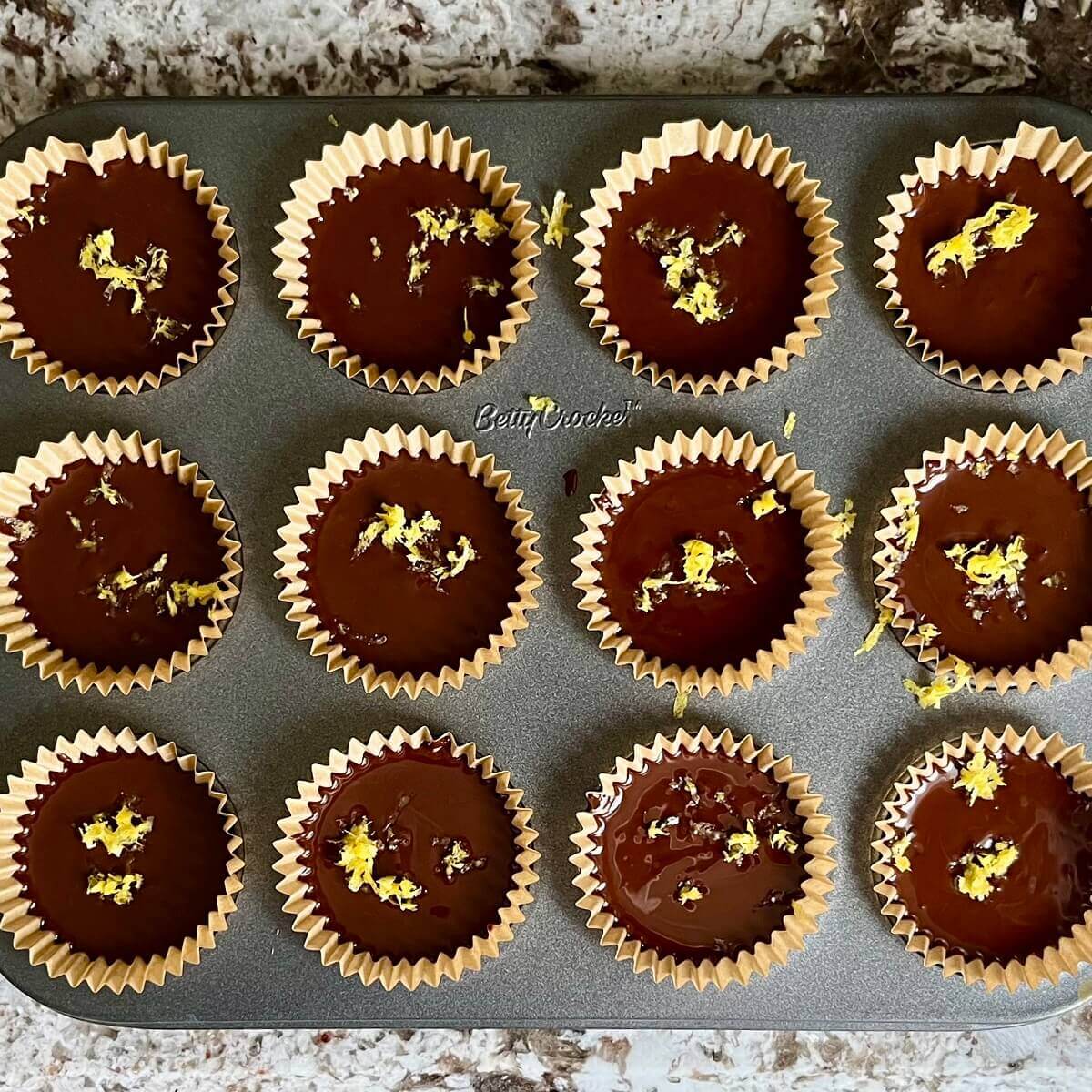 Chocolate treats topped with lemon zest in a mini muffin pan.