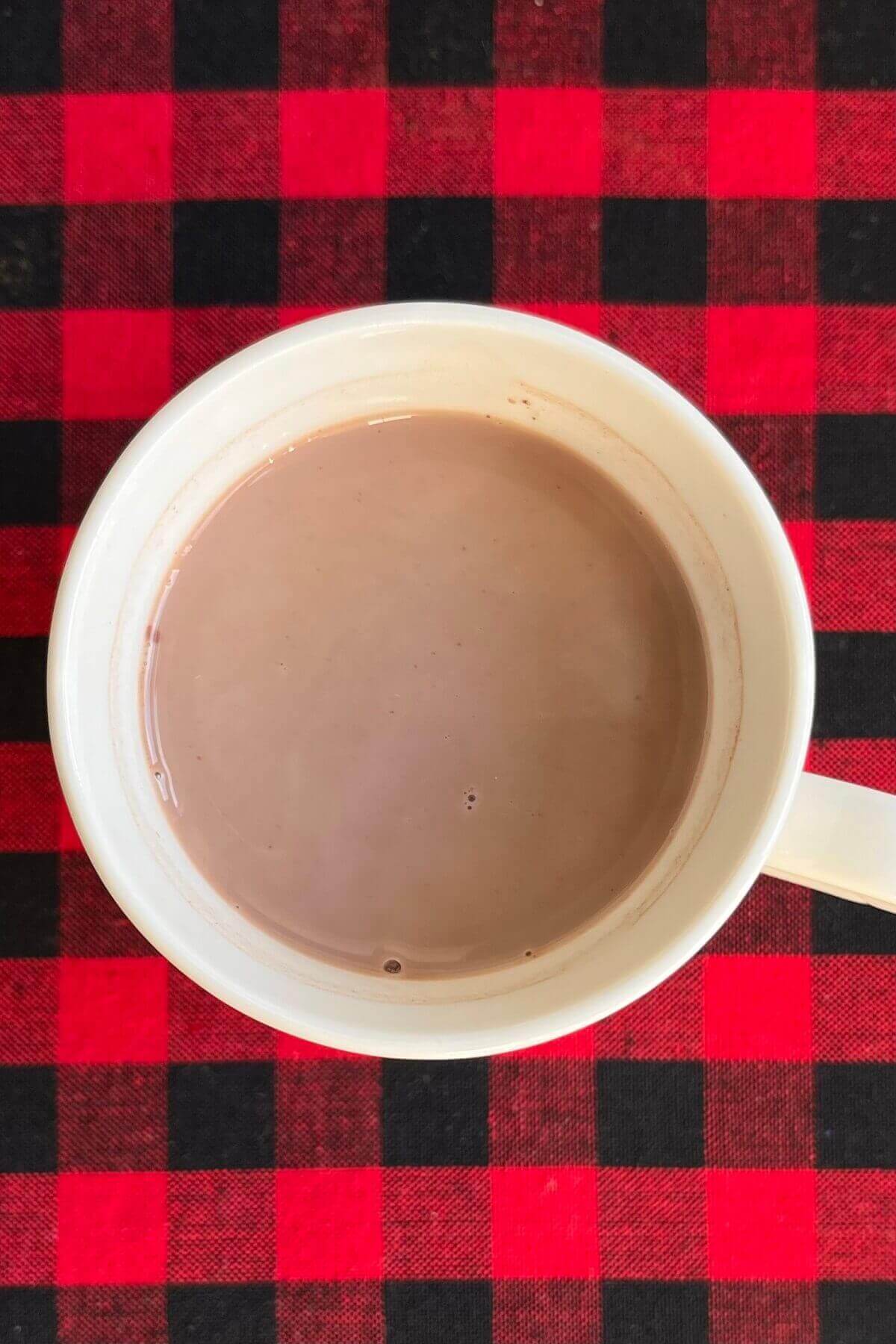 Maple syrup hot chocolate in a white mug on a red gingham placemat.
