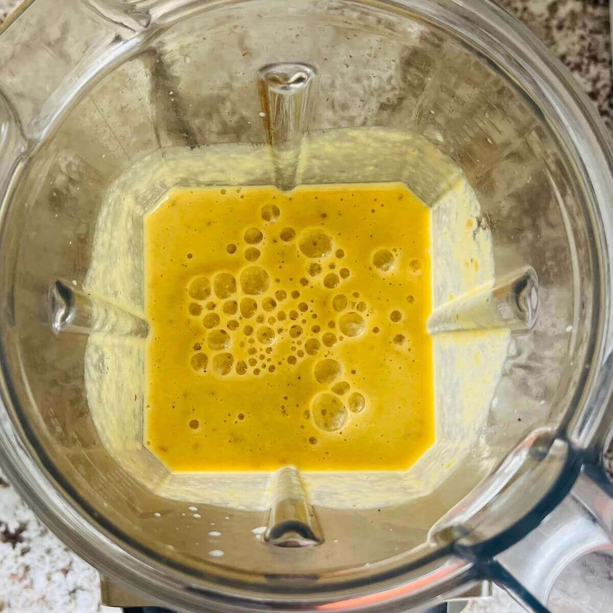 A blended orange colored smoothie in a blender.