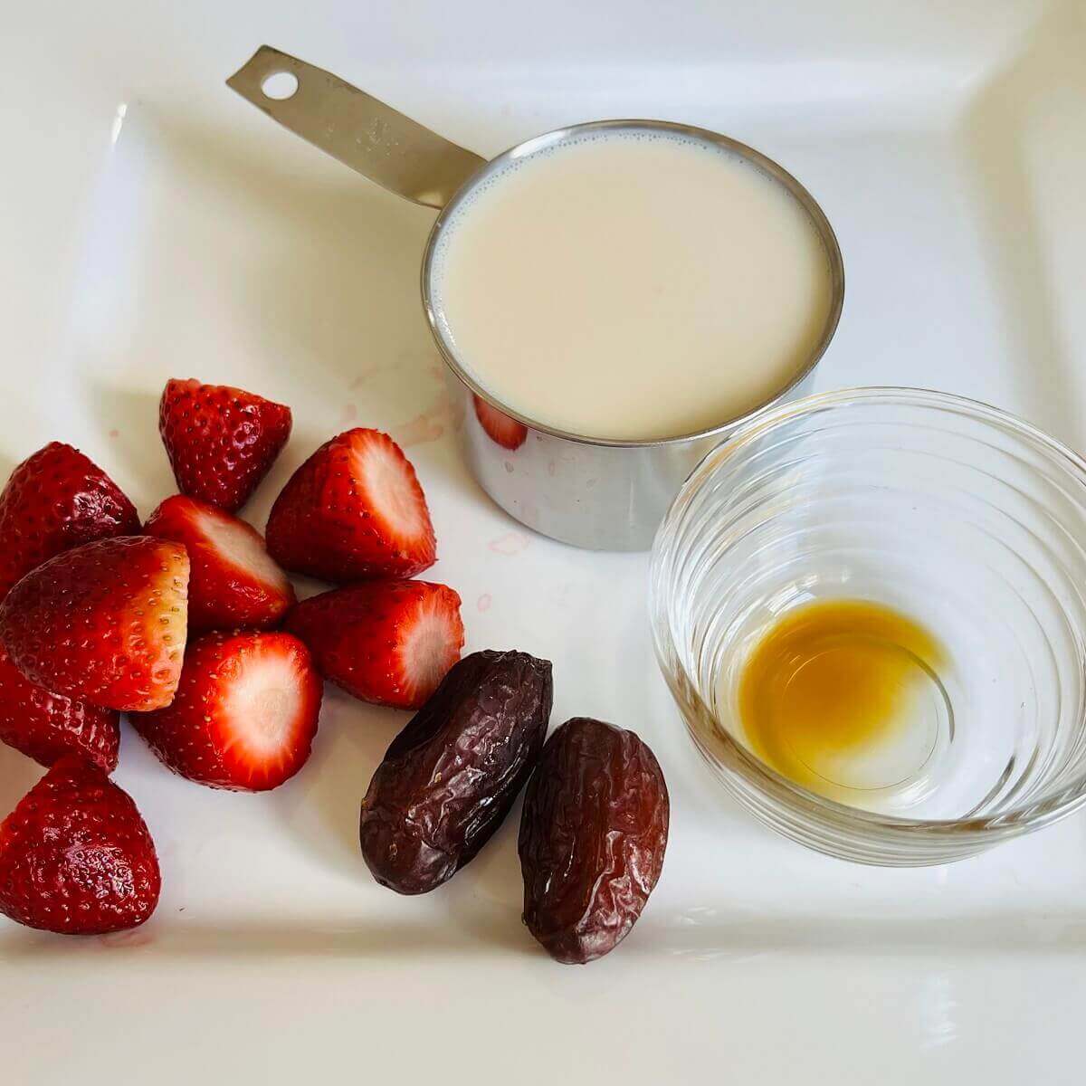 Strawberries, dates, soy milk, and vanilla on a white plate.