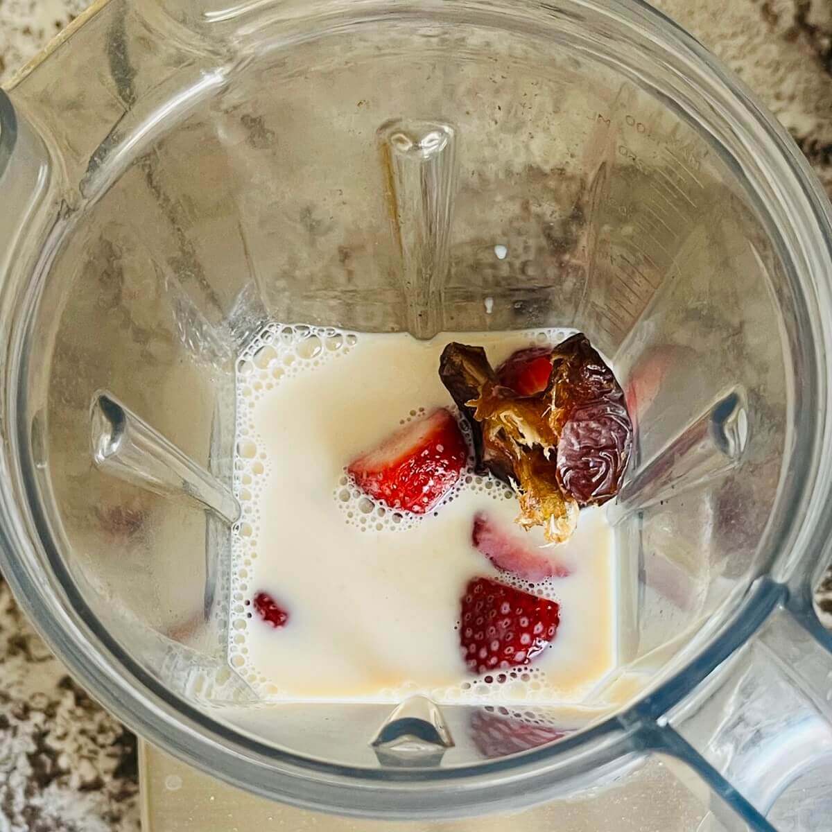 Strawberries and other ingredients for a smoothie in a blender.