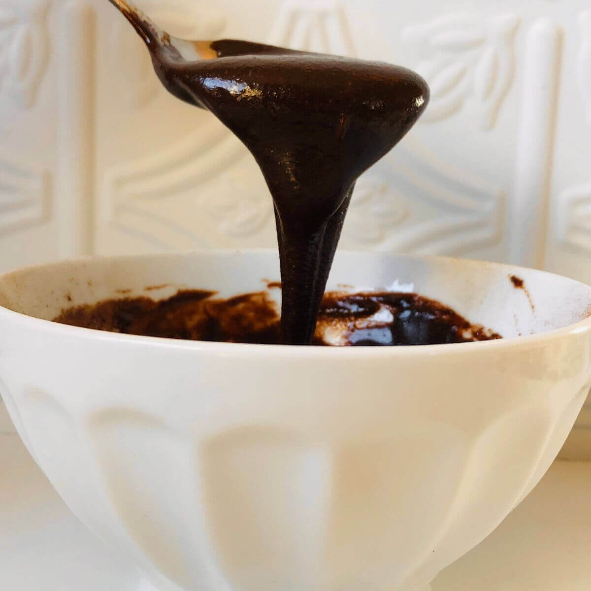 Vegan frosting dripping off a spoon into a bowl.