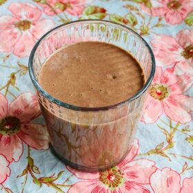 Chocolate walnut smoothie in a glass on a floral placemat.