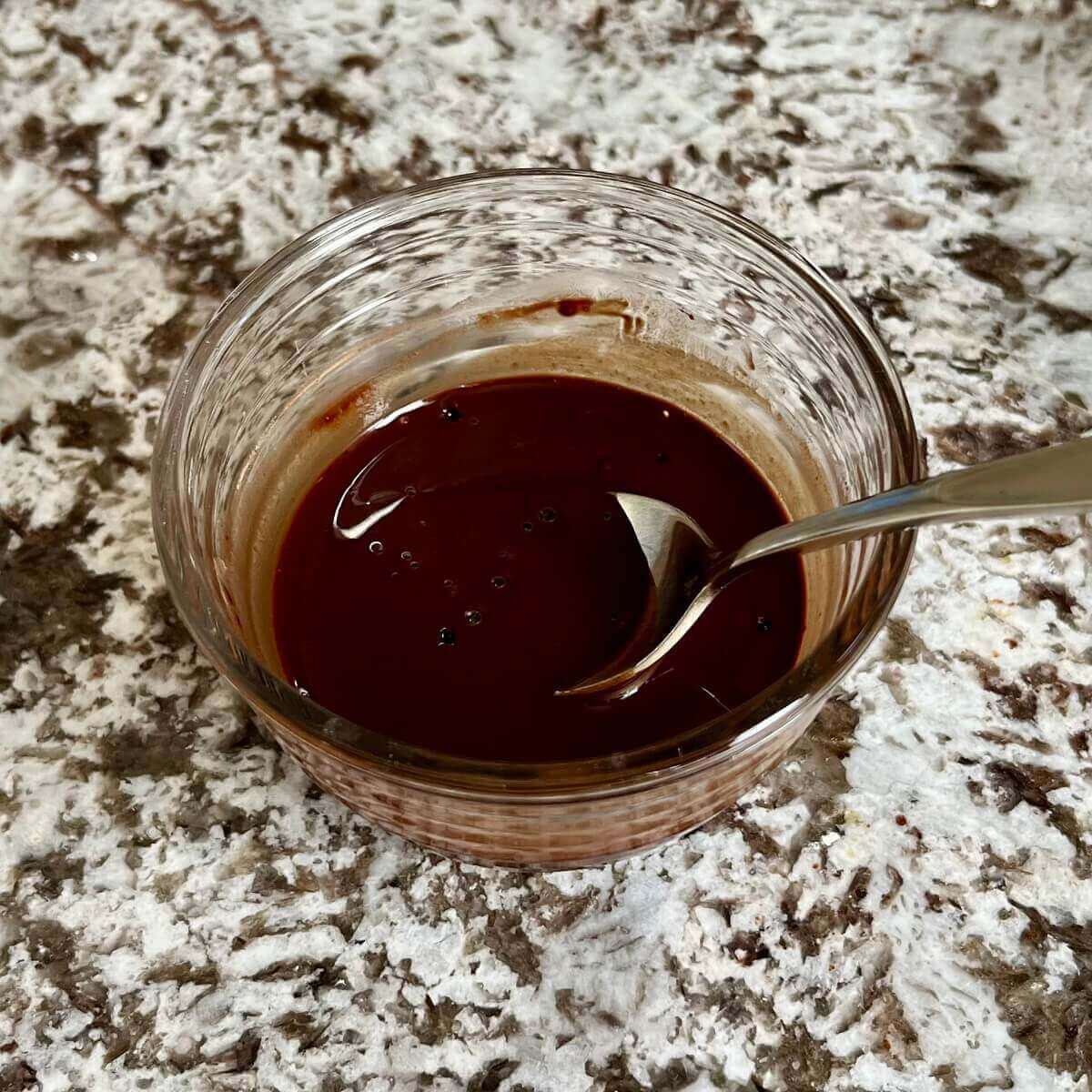 Cocoa powder and coconut sugar dissolved in boiling water in a glass bowl with a spoon.