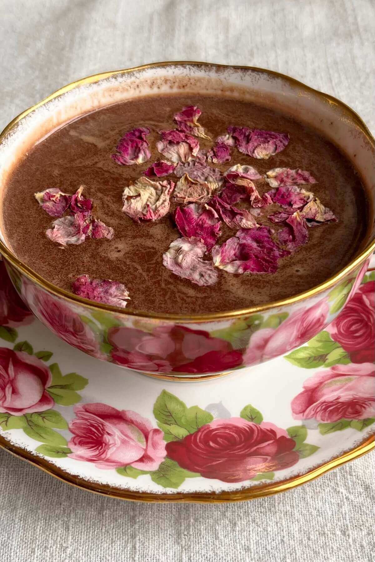 Rose hot cocoa in a teacup with dried rose petals sprinkled on top.