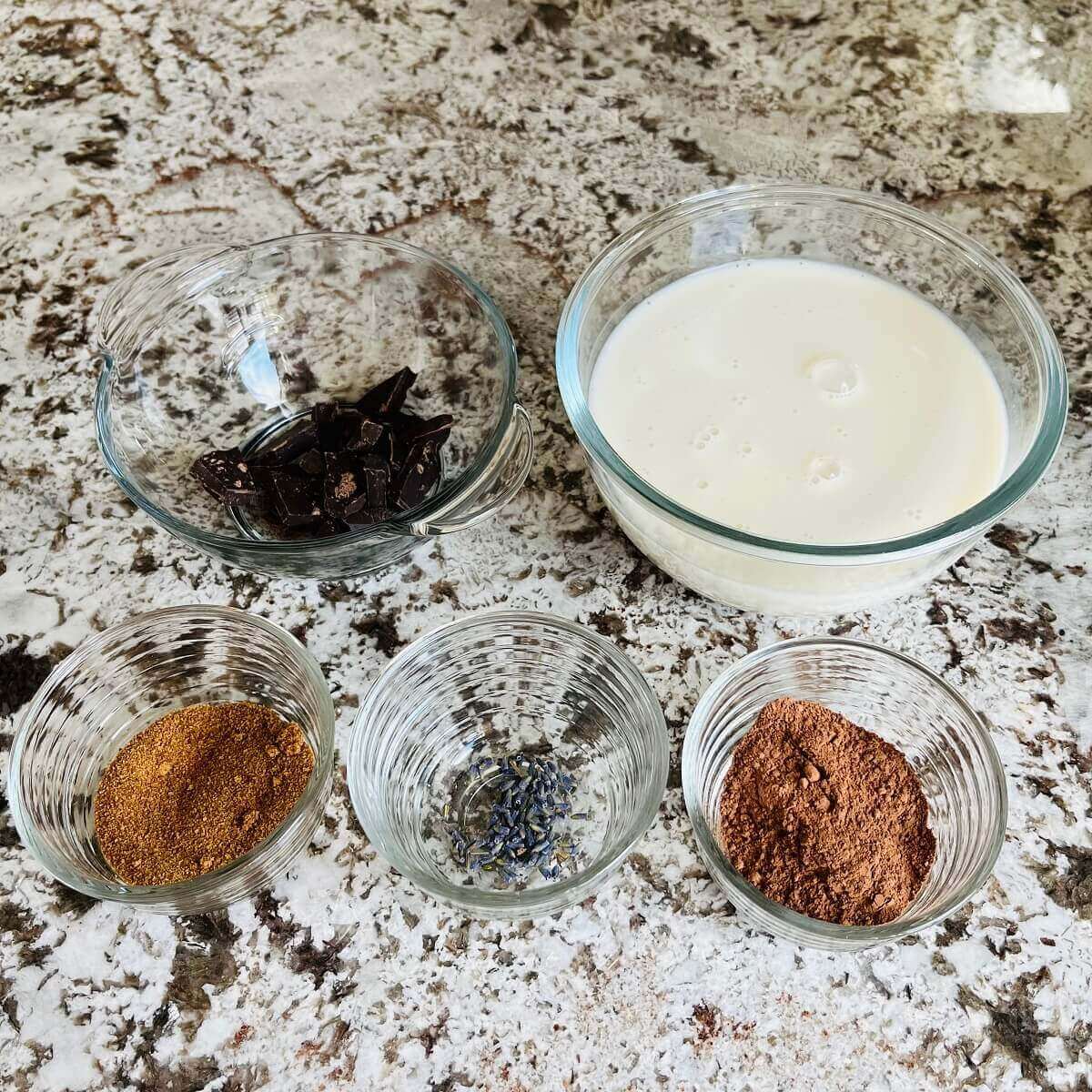 Dried lavender flowers, coconut sugar, cocoa powder, almond milk, and chopped dark chocolate in glass bowls.