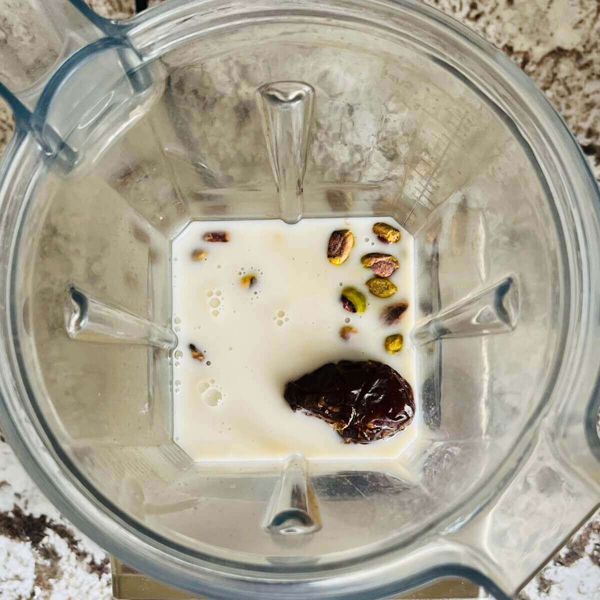 Pistachios, dates, almond milk, and vanilla extract in a blender.