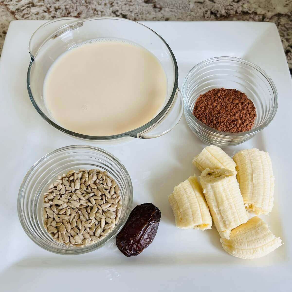 Sunflower seeds and other ingredients for a smoothie on a white square plate.